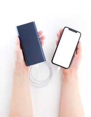 Power bank and smartphone in hands on a white background. The smartphone is charging from the power bank.