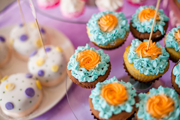 Birthday party concept. Table for kids with cupcakes with blue and orange top and decor items in bright pink and blue colors