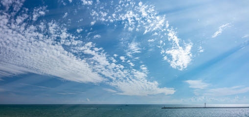 Sky with small clouds over the sea with a breakwater and a beacon