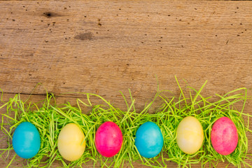 Six colored eggs with Easter greass on barn wood