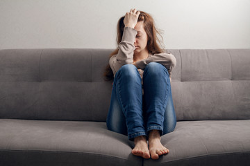 Frustrated girl sitting on the couch with a headache.