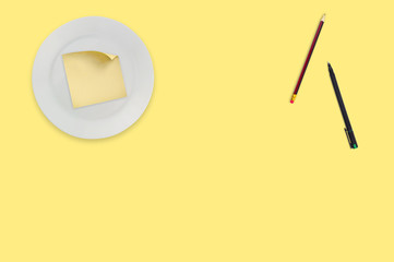 Blank square paper sticker with curved corner in white round plate near wooden pencil and black pen...
