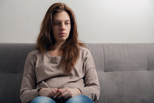  A portrait of a sad girl sitting on a couch.