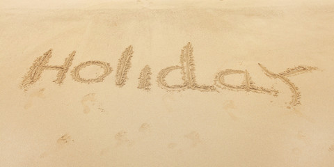 Word Holiday written on wet beach sand.