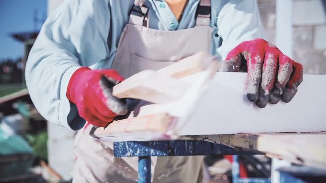 Shaping styrofoam in slow motion. Close up of styrofoam in focus while male worker grinds it, particles flying all around.