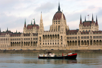 Cargo ship sailing on the Danube. Barge on the background of the Parliament, famous sights of Budapest on a cloudy day.