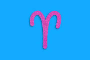 Symbol of astrological sign aries cut out of purple paper in center on blue table. Top view. Horoscope concept