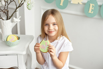 Beautiful child is eating gingerbread eggs. Happy family preparing for Easter.