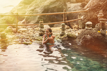 adult girl posing with a smile in the sun and a thermal spring on the background of rocks