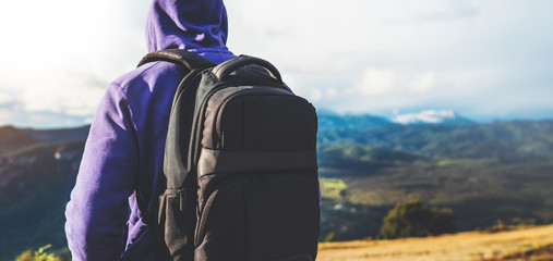 tourist traveler with black backpack on background top mountain, traveler look at blue sky clouds, hiker enjoying nature panoramic landscape in trip, relax holiday mockup concept in trekking trip