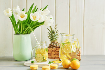 Lemonade and flowers tulips on table. Mason jar glass of lemonade with lemons and straw. Copy space. Fruits and macaroons on the table. The concept of spring and summer season.Healthy Food and Drink