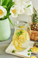 Fototapeta premium Lemonade and flowers tulips on table. Mason jar glass of lemonade with lemons and straw. Copy space. Fruits and macaroons on the table. The concept of spring and summer season.Healthy Food and Drink