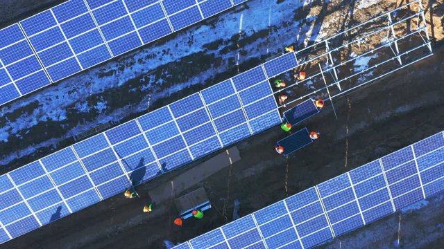 Aerial top rotating view of a group of workers in bright helmets installing solar panels at a solar power station under construction