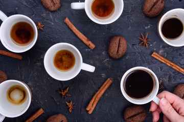Delicious and fragrant coffee in the form of coffee, with grains of coffee. Cups of coffee in beautiful cups. Cinnamon sticks on a black background