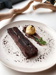  Chocolate dessert cake on a white plate next to wooden twigs