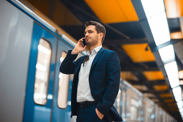 Attractive businessman talking by mobile phone while waiting for train in metro.