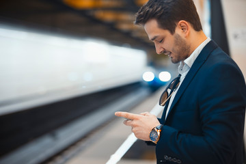 Attractive businessman texting message in mobile phone while waiting for train in metro.