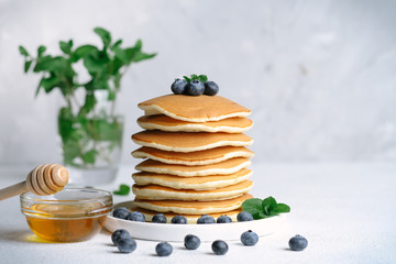 Very hearty tasty breakfast, pancakes with berries, honey and maple syrup on a light background 