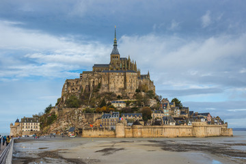 Fototapeta na wymiar Mont Saint Michel, famous and beautiful Island with historical Abbey, panoramatic view from land over the field, cloudy weather, Normandy, northern France
