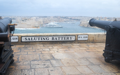 Sign with Saluting Battery lettering on a wall in the Upper Barrakka Gardens heavy guns on both sides. Valletta, Malta, Europe