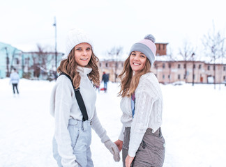 Two female students, an ice rink in winter in a city park. Hold each other's hands learn to ride, women in sports and an active lifestyle. In warm everyday winter clothes.