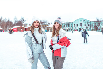 Two female students posing and smiling, ice skating rink in winter in city park. Woman's rest sports and active lifestyle. In warm everyday winter clothes. Concept weekend holiday in winter resort.