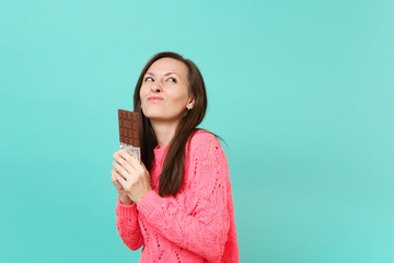 Pretty pensive young woman in knitted pink sweater looking up, hold in hands chocolate bar isolated...