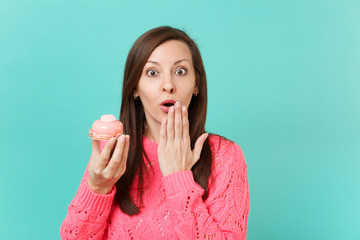 Shocked young girl in knitted pink sweater keeping mouth wide open covering mouth with palm hold in...