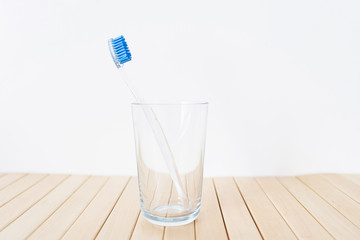 A glass with a plastic toothbrush on white and wooden background
