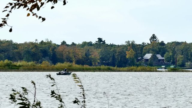 Unidentifiable couple fishing in a boat on a lake in early autumn.