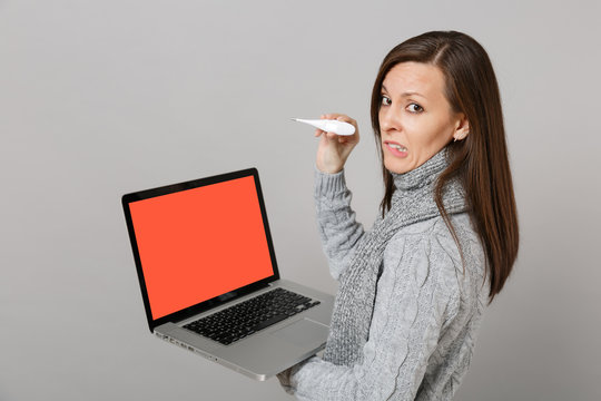 Side View Of Puzzled Woman In Sweater Scarf Hold Thermometer, Laptop Pc Computer With Blank Empty Screen Isolated On Grey Background. Healthy Lifestyle Online Treatment Consulting Cold Season Concept.