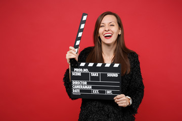 Laughing young woman in black fur sweater hold classic black film making clapperboard isolated on...