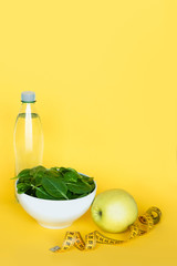 Concept diet - healthy food. Water, spinach, apple and tape line on yellow background. Copy space