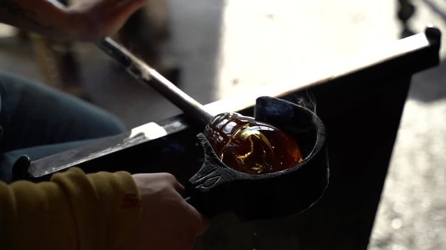 A glass blower rolling a piece of hot molten glass using a tool
