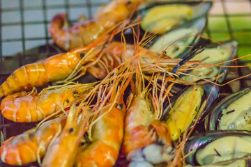 Grilled shrimps and green mussels on charcoal stove at night party. Seafood barbecue party with shrimps and green mussels are grilling on fire. Seafood BBQ concept, selective focus.