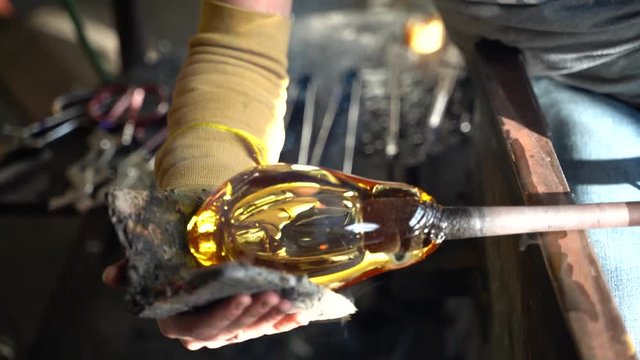 A glass blower rolling a piece of hot molten glass by hand
