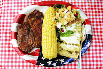 Beef steak, corn, salad and baked potato on papper plate
