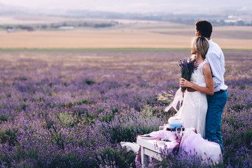 At sunset in a lavender field, the bride and groom stand at the table set for dinner