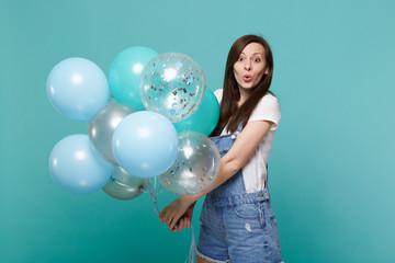 Portrait of surprised amazed young woman in denim clothes celebrating and holding colorful air...