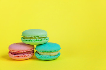 Obraz na płótnie Canvas Sweet almond colorful unicorn pink blue yellow green macaron or macaroon dessert cake isolated on trendy yellow modern fashion background. French sweet cookie. Minimal food bakery concept. Copy space