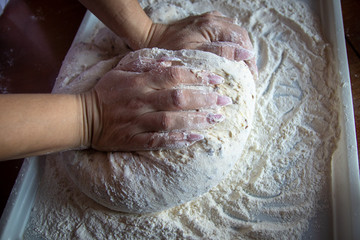 Woman's hands with manicured nails work with dough in the kitchen. Kneading homemade dough with flour for bread, pastry or pizza.