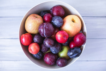Plum and apples in bowl on a wooden table top view.
