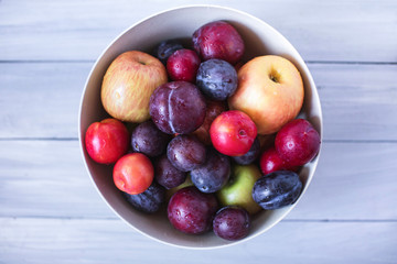 Plum and apples in bowl on a wooden table top view.