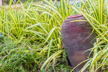 Green garden decoration with clay pottery fountain. Old clay jar in the garden wit h green plants leaves background. Porcelain pitcher decoration in the green-yellow leaves garden.