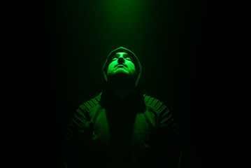Guy wearing a Black Jumper in a Dark Room .Green Light on Face.
