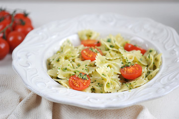 Farfalle pasta with green pesto and cherry tomatoes. The composition is complemented by a cloth napkin and cherry tomatoes. Light background. Close-up. Macro shooting.