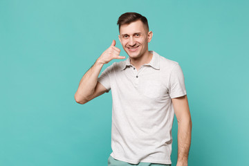 Handsome young man in casual clothes standing and doing phone gesture like says call me back isolated on blue turquoise wall background. People sincere emotions, lifestyle concept. Mock up copy space.