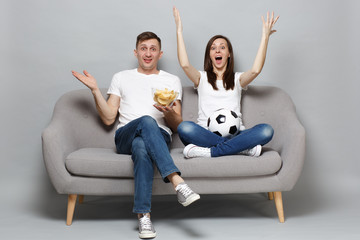 Excited couple woman man football fans cheer up support favorite team with soccer ball, holding bowl of chips sreading rising hands isolated on grey background. Sport family leisure lifestyle concept.