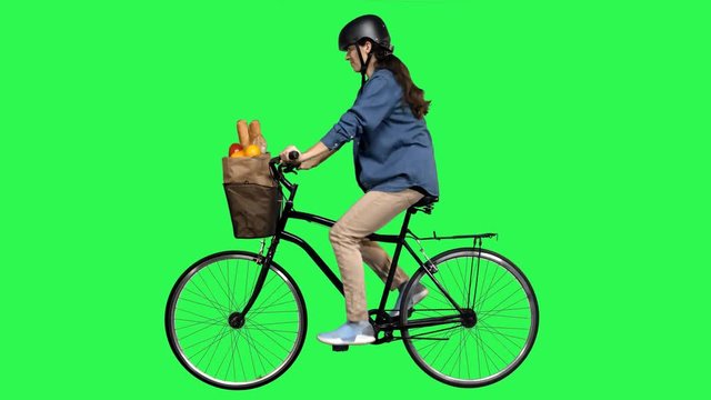 Safety first woman riding a bicycle over a green screen, looking around, wearing a helmet. No motion blur for optimal keying.