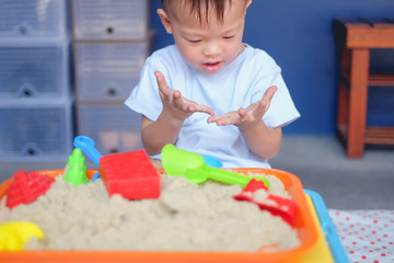 Cute smiling Asian 2 - 3 years old toddler boy playing with kinetic sand in sandbox at home /...